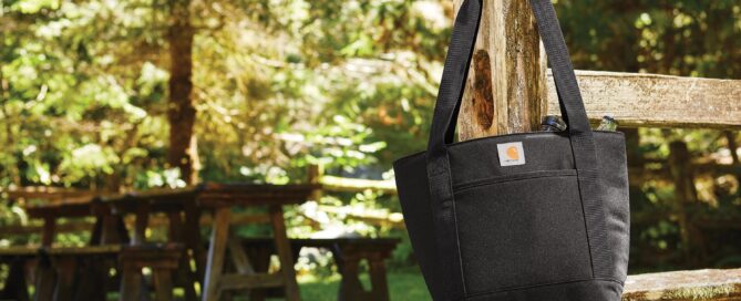 Picture of tote bag hanging on a fence post and a picnic table in the background
