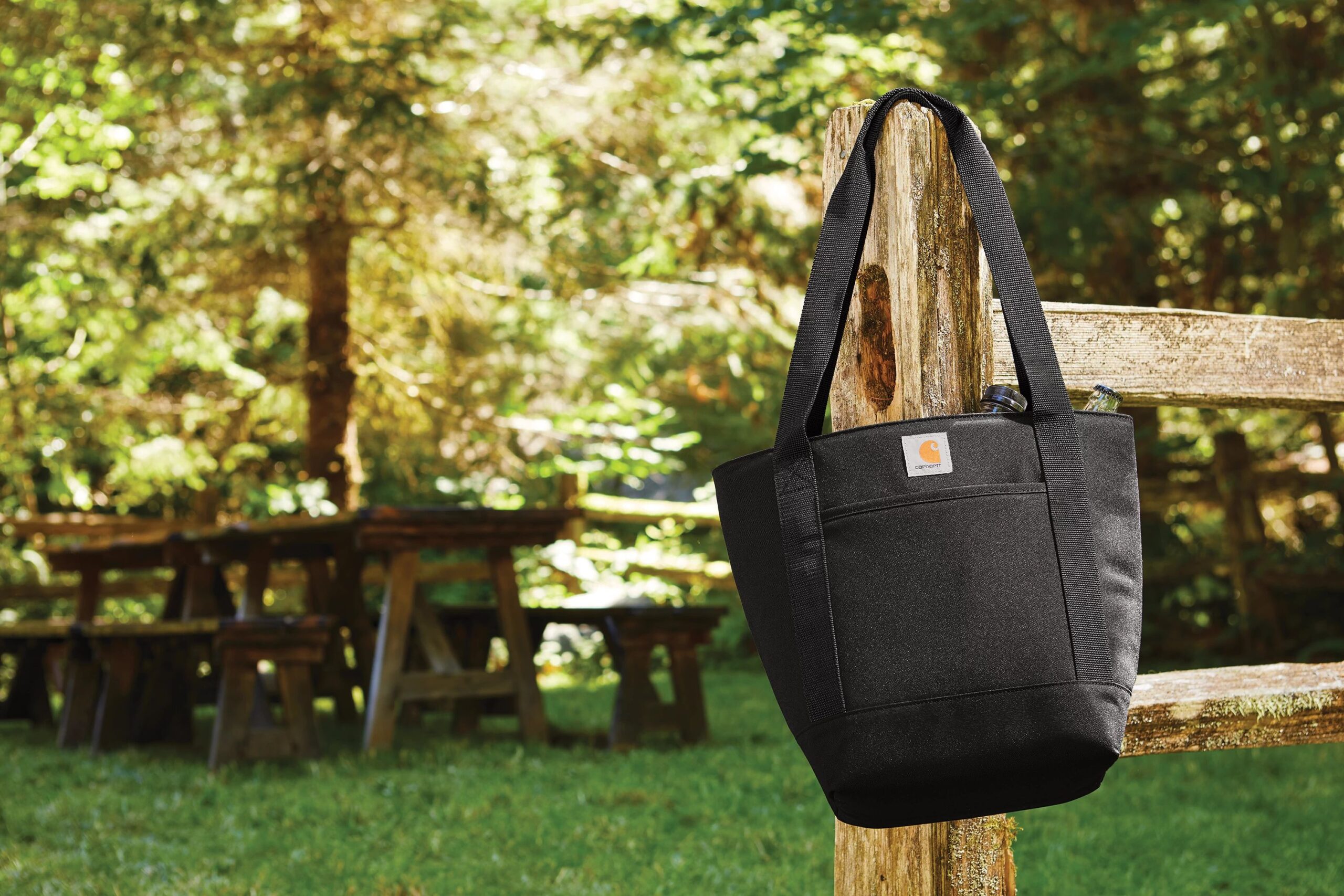 Picture of tote bag hanging on a fence post and a picnic table in the background